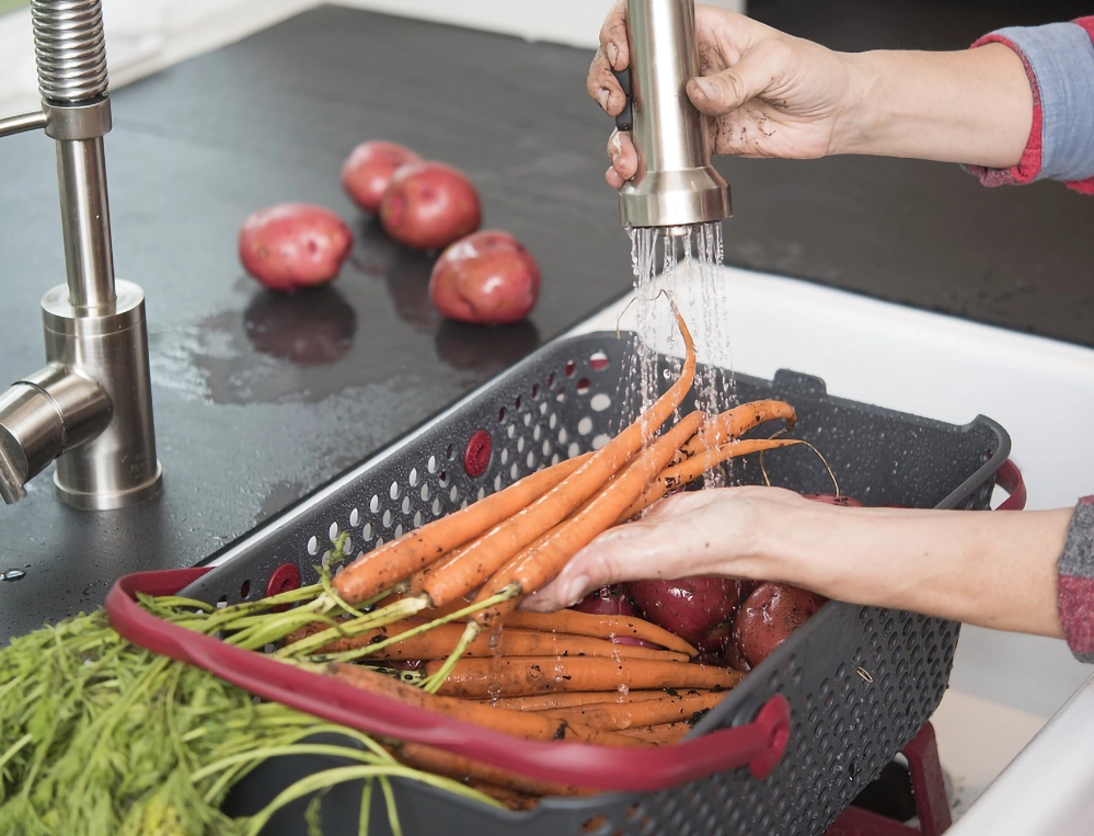 Hands rinsing fresh garden carrots and potatoes in a harvest basket under a kitchen faucet 