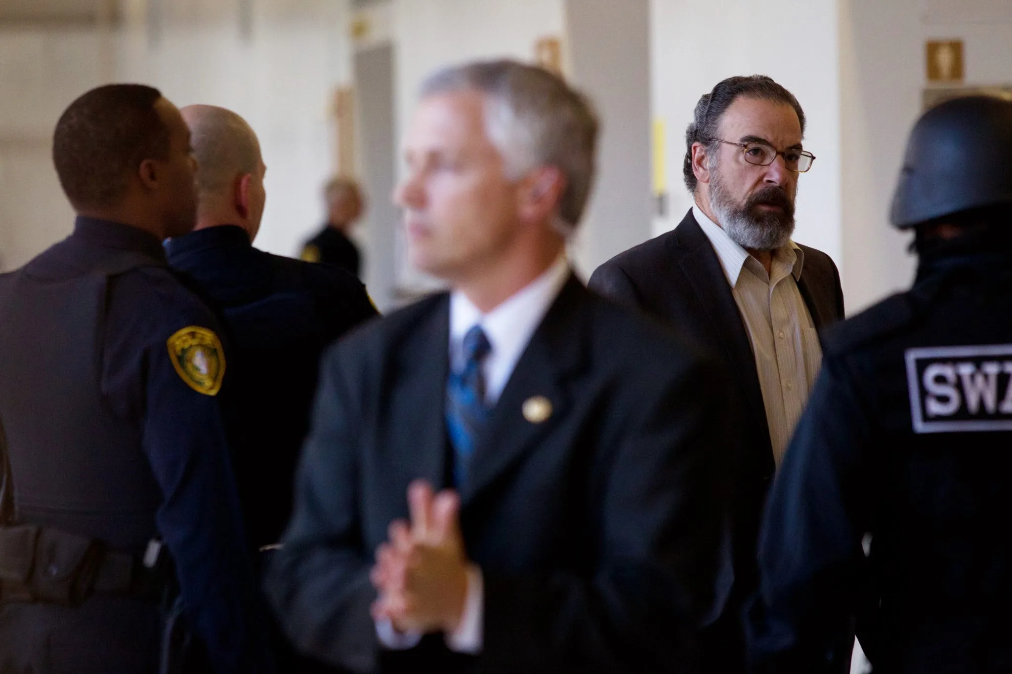 Mandy Patinkin as Saul Berenson in Homeland, standing alert in a corridor surrounded by law enforcement