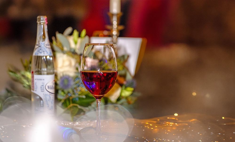 Glass of red wine on a wooden table, soft floral arrangement and warm candlelight in the background