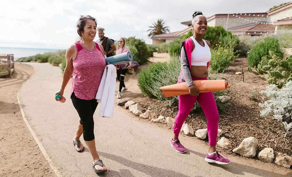 Diverse group of older women walking together on a coastal path carrying yoga mats after an outdoor class