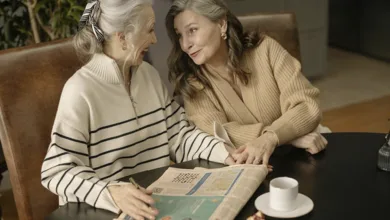 Two older women laughing together over a crossword puzzle and coffee at a café table