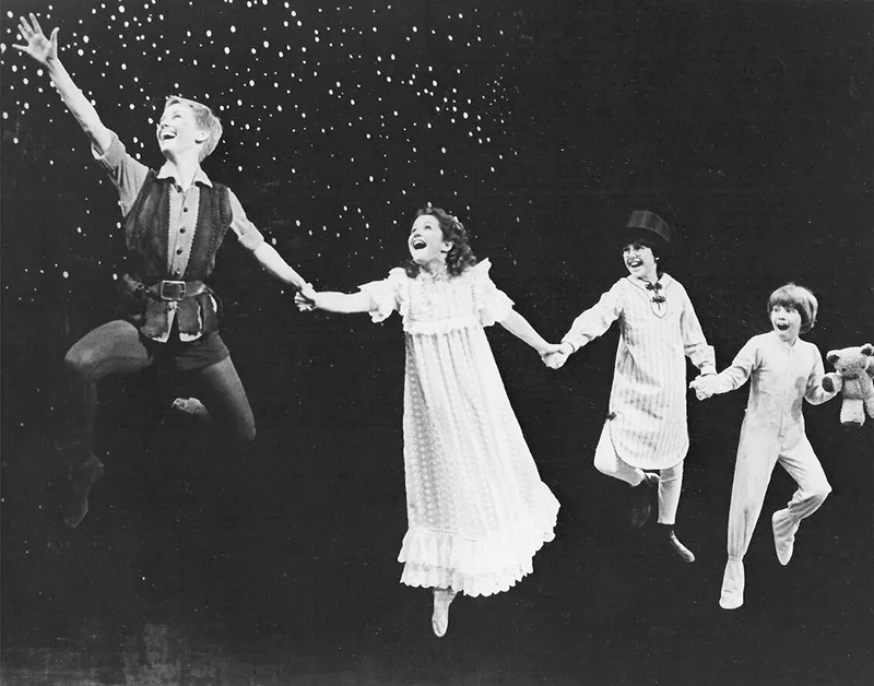 Sandy Duncan as Peter Pan flying on stage, hand-in-hand with Wendy, John, and Michael Darling, black and white production photo