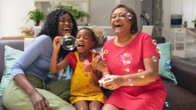 Grandmother, mother and granddaughter laughing and blowing bubbles together on the couch