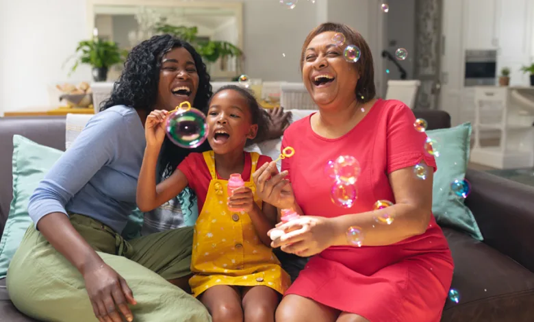 Grandmother, mother and granddaughter laughing and blowing bubbles together on the couch