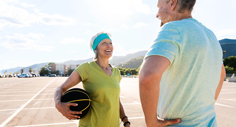 Active senior couple laughing and playing basketball outdoors