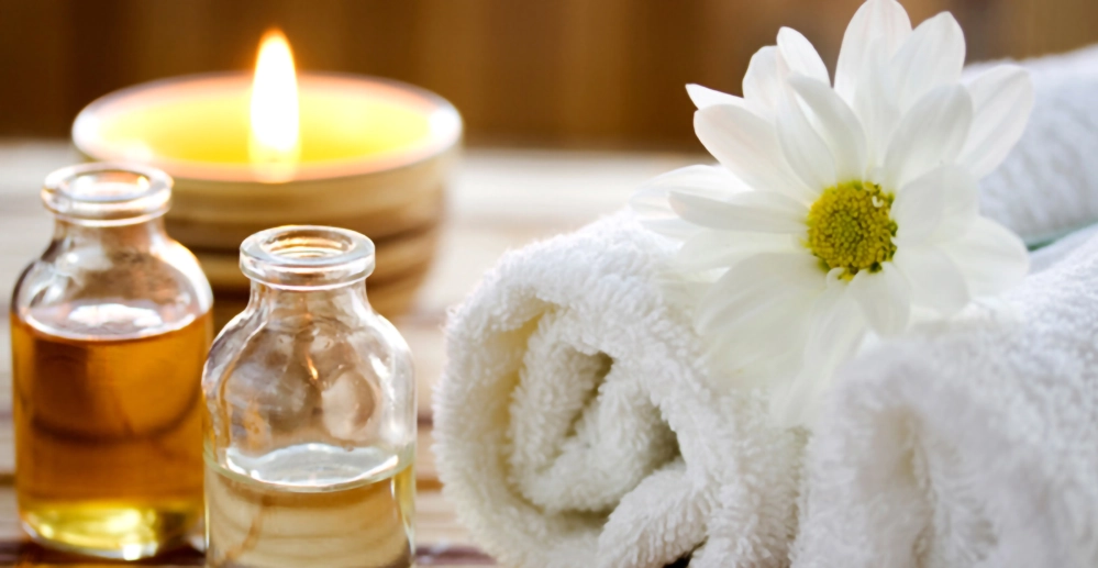 Mother's Day at-home spa setup with candle, essential oil bottles, towel, and a white daisy
