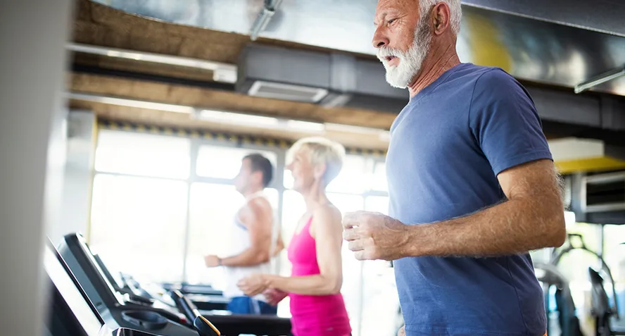 People 50+ on Treadmills Active adults on treadmills at a gym smiling and exercising together