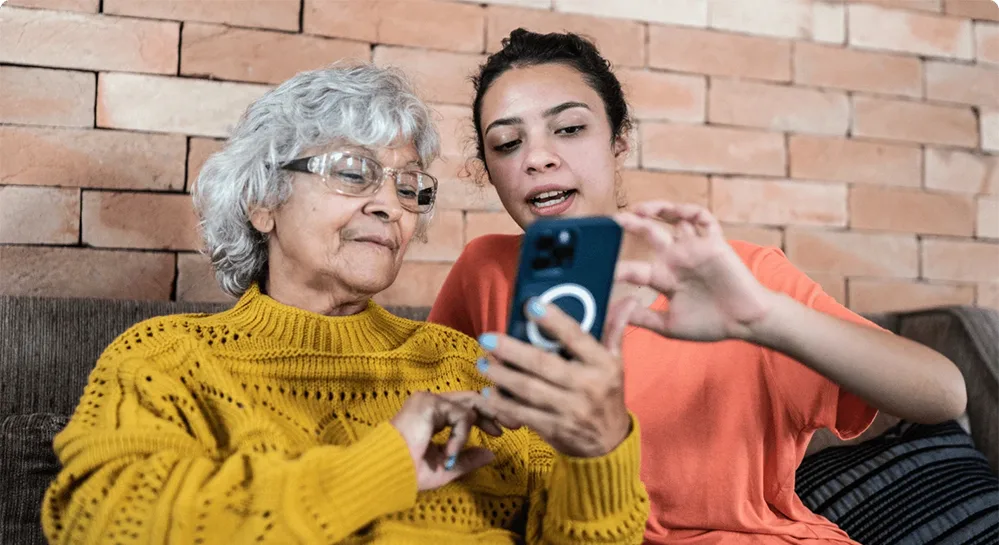 5 Ways You Can Support Seniors in Your Local Community 4 At a 50+ tech fair, a young adult helps an older woman explore her phone’s features and functions.