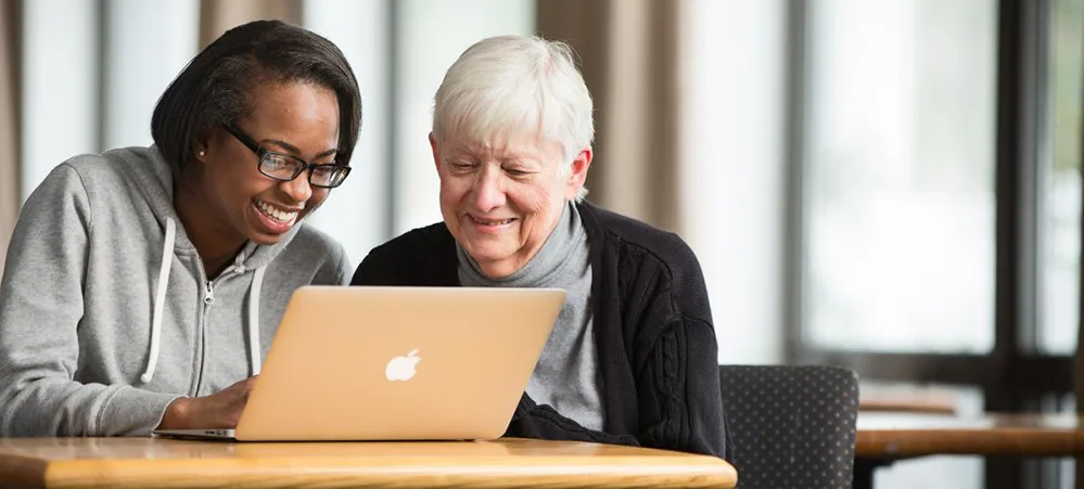 5 Ways You Can Support Seniors in Your Local Community 3 Younger woman teaching an older adult how to use a laptop during a technology support session.