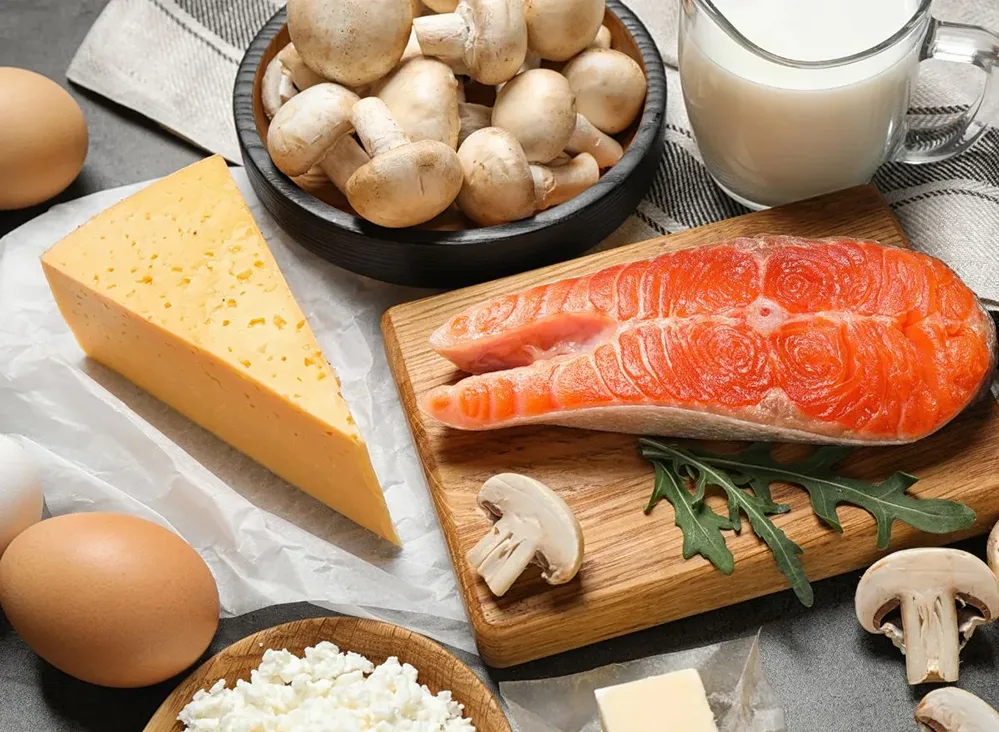 How to Boost Your Vitamin D Levels Naturally—All Year Long 2 Assortment of vitamin D-rich foods, including salmon, eggs, cheese, milk, and mushrooms, on a kitchen counter.
