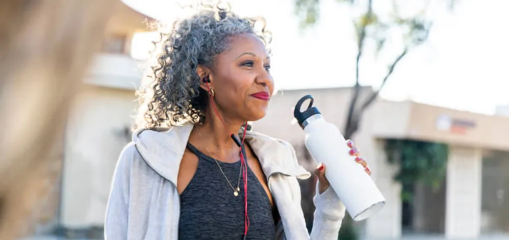 Top 4 Restful Sleep Strategies Tailored for the 50+ Body 4 Older woman walking with a water bottle in hand during a morning routine to support sleep.