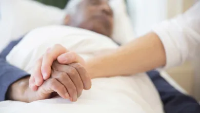 Improving Post-Hospital Outcomes for Older Adults 3 Older adult patient resting in a hospital bed, visitor holding his hand in support.