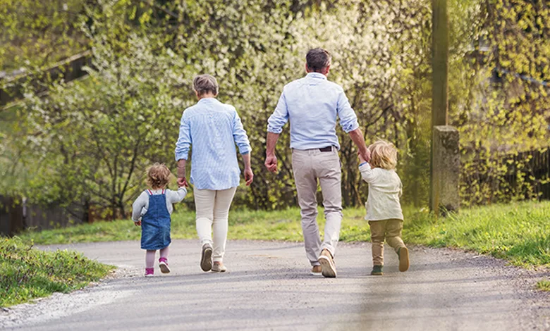 Are Grandparents the Answer to America's Childcare Crisis? 1 Grandparents walking hand-in-hand with toddler grandchildren on a country road in spring, symbolizing multigenerational support in childcare.
