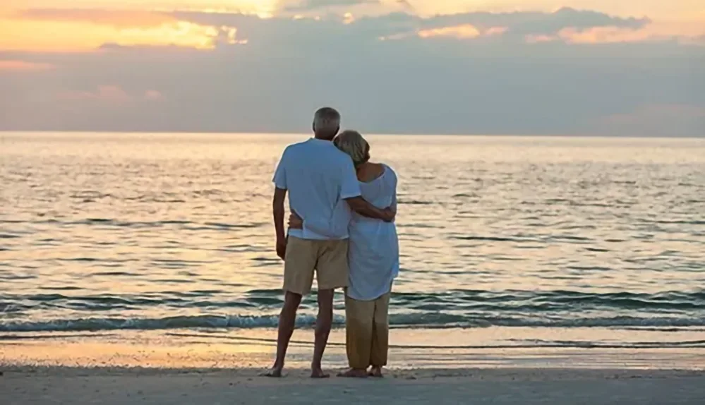 Honoring a Loved One with Ocean Ash-Scattering 3 An older couple stands on the shore at dusk, arms around each other, looking out over the ocean during an ash-scattering ceremony.