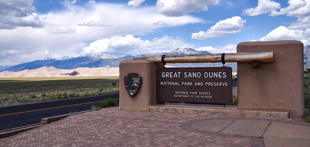 Take a Hike! Burning Sand and Towering Dunes: A Great Hike in Colorado 3 Entrance sign to Great Sand Dunes National Park and Preserve with dunes and mountains in the background.