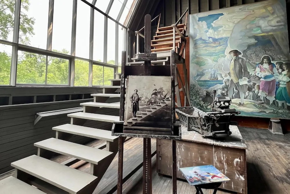 Explore Brandywine Valley: Gardens, Art, Covered Bridges & History 4 Interior of N.C. Wyeth’s preserved painting studio in Brandywine Valley, featuring easels, a staircase, natural light, and historical murals in progress.