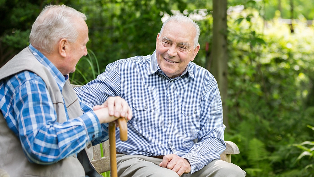 The Circle That Sustains Us 5 Two senior male friends sitting on a park bench, talking and enjoying each other’s company.