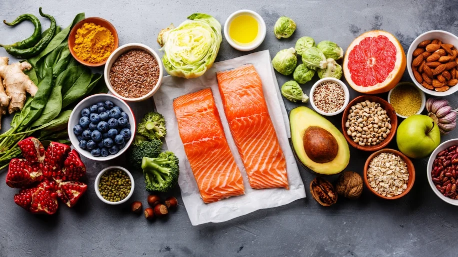 6 Essential Tips for Knee Replacement Recovery at Home After 50 2 Anti-inflammatory foods for knee surgery recovery, including salmon, berries, leafy greens, nuts, and olive oil on a grey surface.