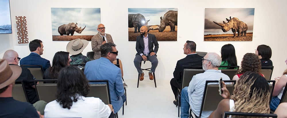The Eye of the Wild 2 The speaker presents Mital Patel's wildlife photography to a seated audience at the Dallas gallery exhibition, with large animal portraits displayed on white walls.