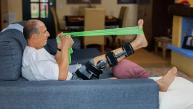 6 Essential Tips for Knee Replacement Recovery at Home After 50 2 Man recovering from knee replacement surgery doing physical therapy exercises with green resistance band while wearing knee brace in rehabilitation setting