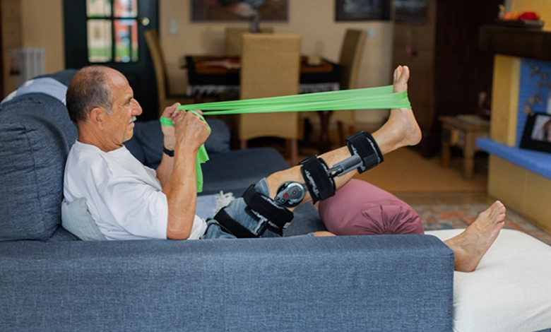 6 Essential Tips for Knee Replacement Recovery at Home After 50 1 Man recovering from knee replacement surgery doing physical therapy exercises with green resistance band while wearing knee brace in rehabilitation setting