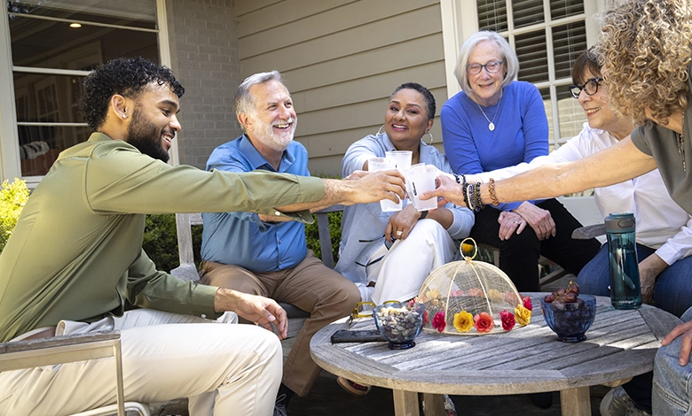 The Circle That Sustains Us 1 Five diverse adults of different ages raising cups in a toast together on an outdoor patio, representing intergenerational friendship and community support