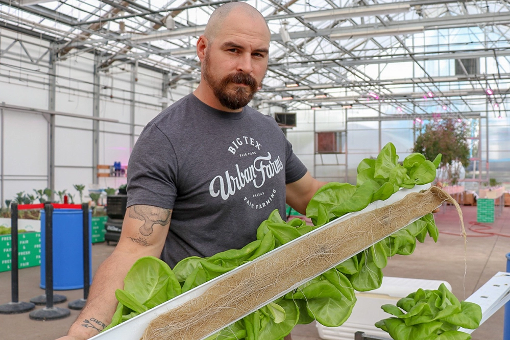How Your Visit to the State Fair of Texas Benefits Communities 3 Robert Blackman holding a large lettuce grown in an NFT hydroponic system at Big Tex Urban Farms greenhouse.