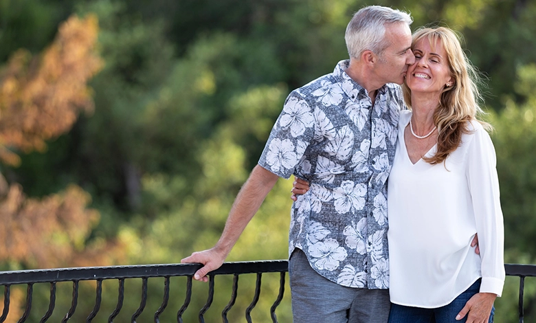 6 Secrets to Long-Term Relationships That Last After 50 1 Mature couple showing affection with man kissing woman's cheek outdoors, demonstrating long-term relationship intimacy.