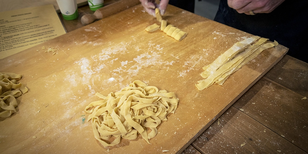 3 Hidden Culinary Gems in Tuscany 3 Hands shaping fresh pasta on a wooden board during a cooking class at Crimson Cat Studios in Tuscany.