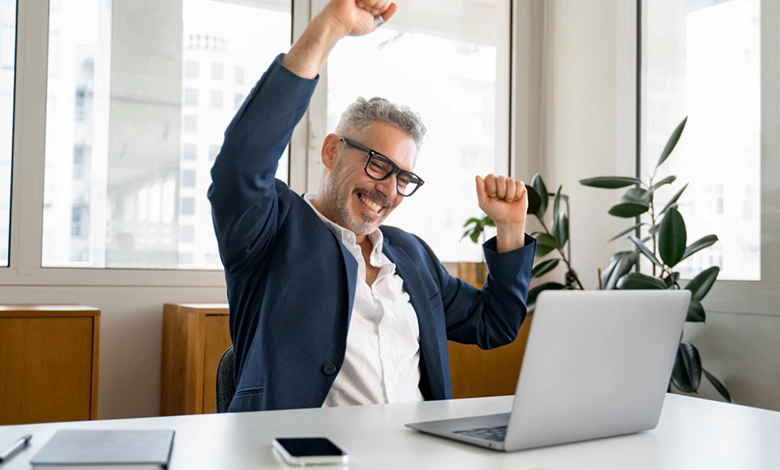 How To Build a Diverse Investment Portfolio in Your 50s 1 Confident businessman in his 50s celebrating success at laptop in modern office