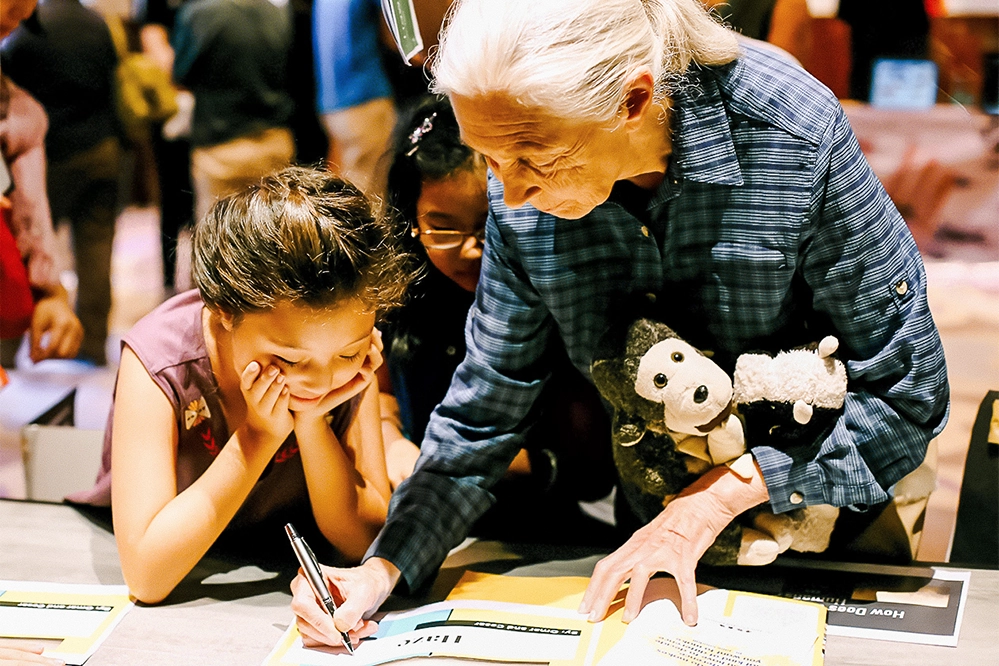 Jane Goodall, Pioneering Chimpanzee Researcher, Dies at 91 4 Jane Goodall with stuffed chimpanzee engaging with young environmental advocates at Roots and Shoots program event