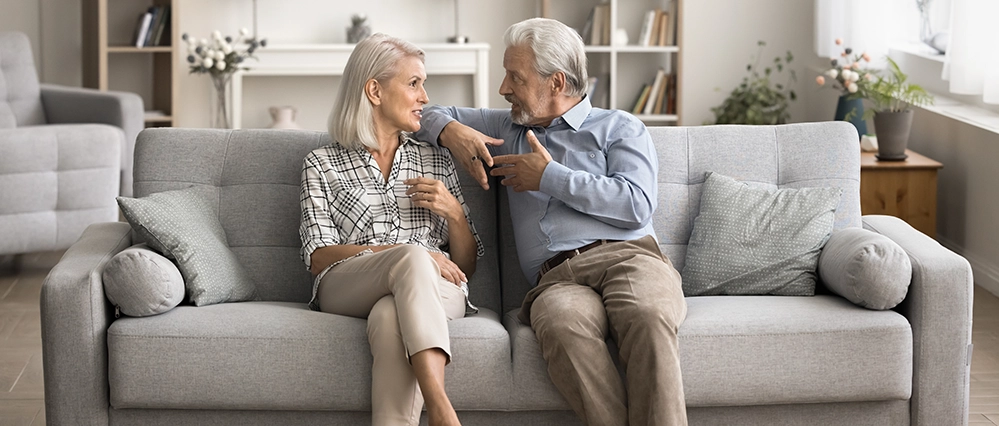 Communication Hacks for Tough Relationships After 50 3 A mature couple sitting together on a sofa, smiling and talking calmly, representing how to keep communication focused on long-term relationship goals after 50.
