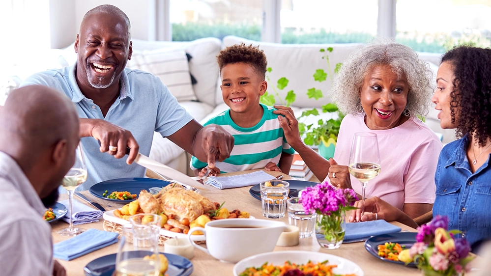 How to Create a Comfortable Home for Multigenerational Living 3 Three generations sharing family meal together at dining table in multigenerational home with grandparents, parents, and child