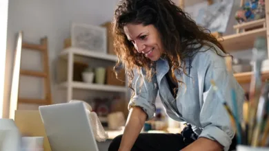 How Facebook Groups Are Helping Parents Navigate the Empty Nest Transition 1 A smiling woman with curly brown hair in a light blue shirt, accessing a college parent group on her laptop.