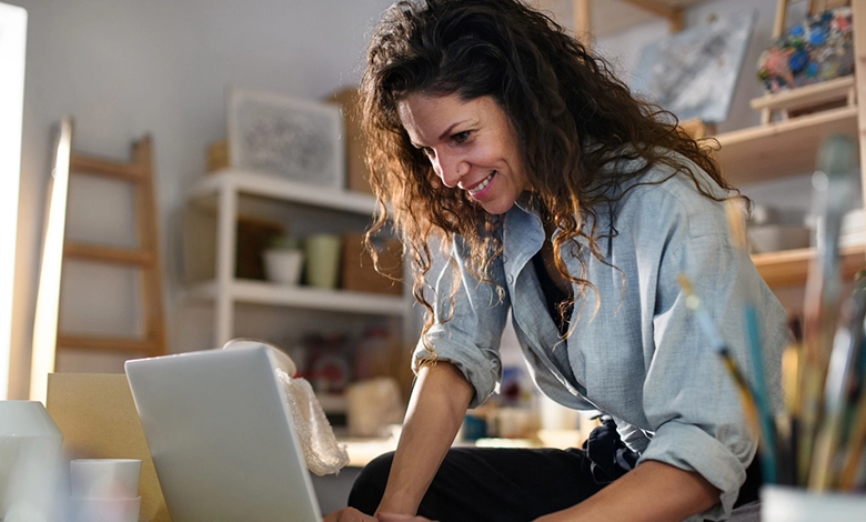 How Facebook Groups Are Helping Parents Navigate the Empty Nest Transition 1 A smiling woman with curly brown hair in a light blue shirt, accessing a college parent group on her laptop.