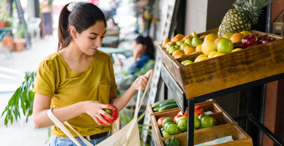 Living Greener for your Grandchildren 3 Young woman with reusable bag shopping for fresh produce, representing next-generation sustainable living practices