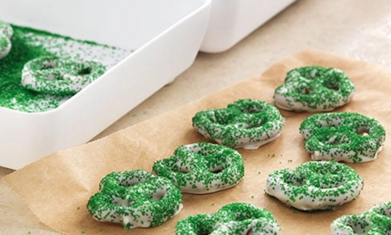 White chocolate–dipped pretzel twists decorated with green sprinkles on parchment paper