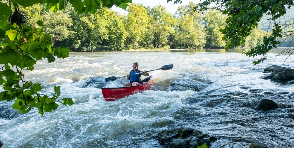 Kayaking Virginia's Blue Ridge After 50: Upper James River 2 Woman kayaking red canoe through Class II whitewater rapids on Upper James River in Virginia's Blue Ridge with rocks and rushing water