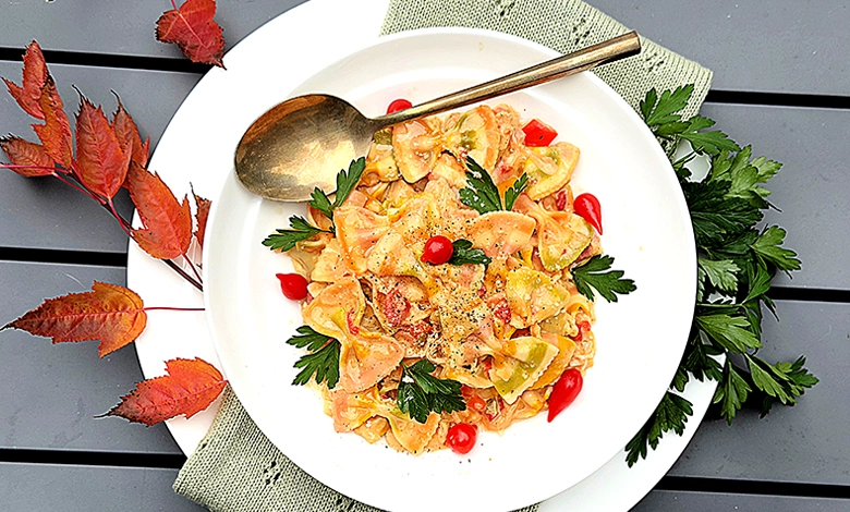 Creamy chicken artichoke bow tie pasta in white bowl with cherry tomatoes parsley garnish and autumn leaves
