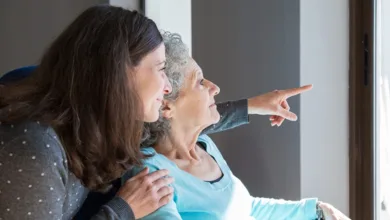 Dementia Caregiver Tips for Families: The Journey Ahead 1 Adult daughter standing close behind elderly mother in wheelchair pointing forward together showing dementia caregiving support and connection