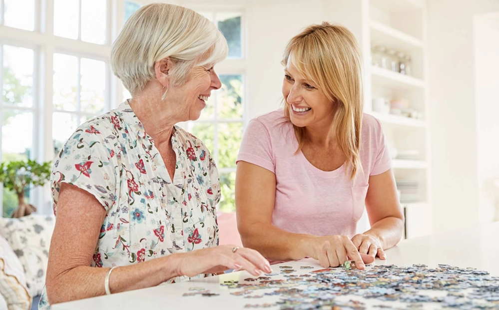 Adult daughter and elderly mother working together on jigsaw puzzle showing cognitive and sensory engagement for dementia care