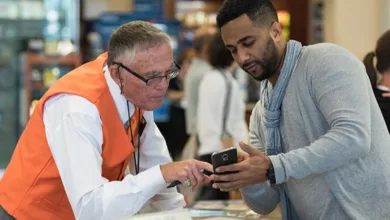 DFW Airport Ambassador in an orange vest helps a male traveler with a mobile device at the airport information center.