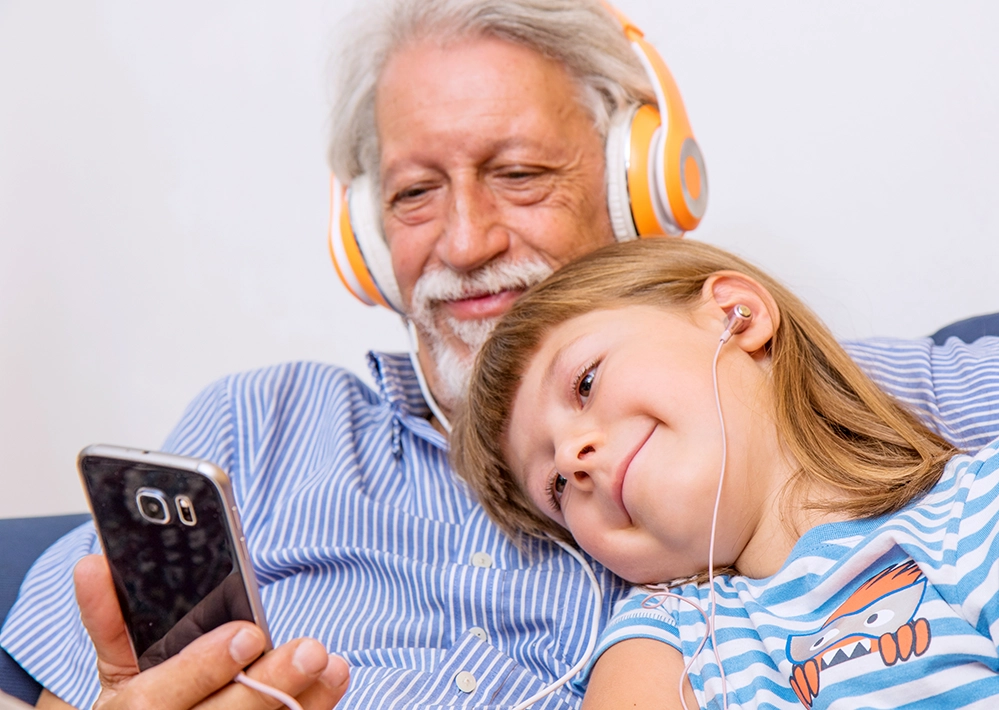 Grandfather and grandson sharing headphones listening to podcast together on phone demonstrating intergenerational bonding through audio content