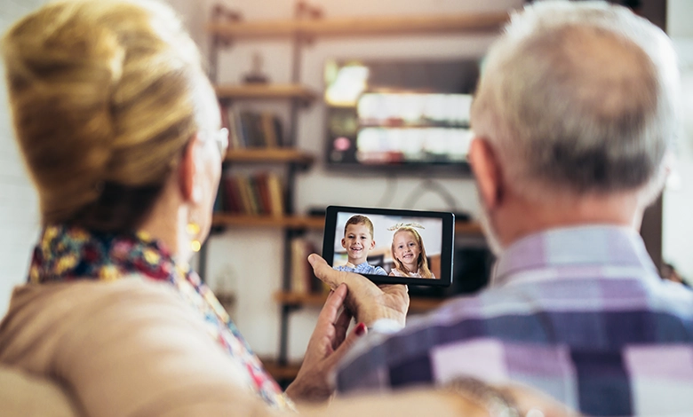 Senior couple on video call with smiling grandchildren on tablet demonstrating long-distance grandparenting and digital family connection