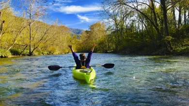 Kayaker with raised arms paddling bright green kayak on James River in fall with mountains and golden foliage in Botetourt County Virginia