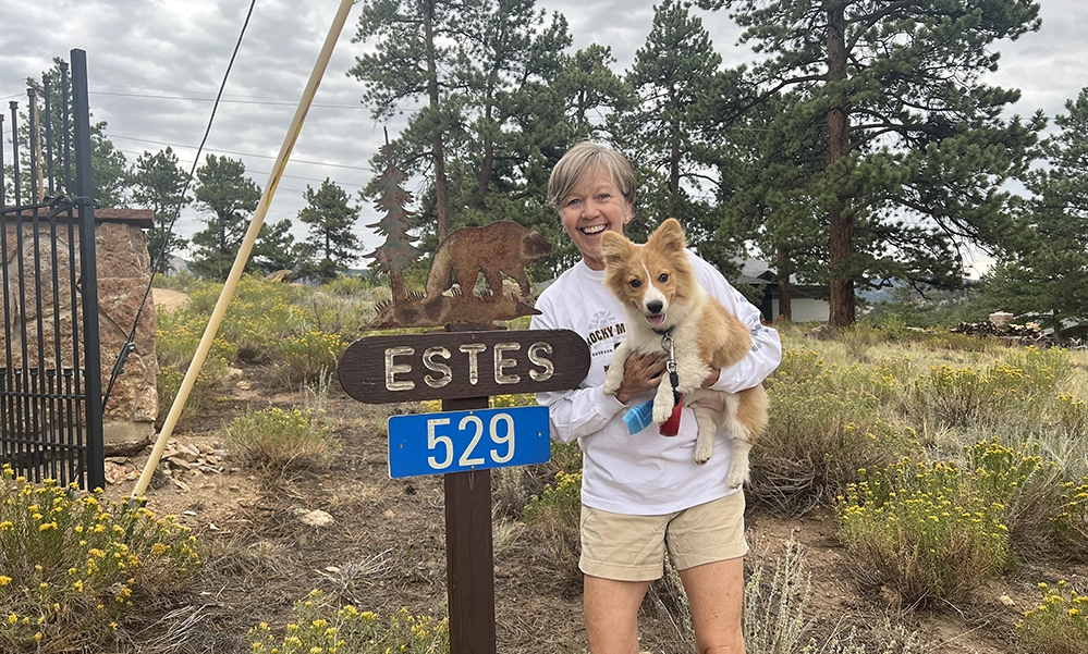 Pets After 50: They're Not Just Companions—They're Lifelines 5 Jeanne Wilgus holding her corgi Estes at Estes Park sign, both smiling—capturing the deep bond between pets and their people.