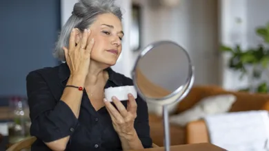 Winter Skin Revival: 10 essential products to keep your glow all season 2 Mature woman with gray hair applying moisturizing face cream while looking in mirror showing winter skincare routine for healthy aging skin