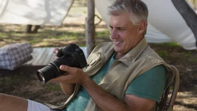 Active senior man using DSLR camera outdoors while camping, enjoying photography hobby after retirement