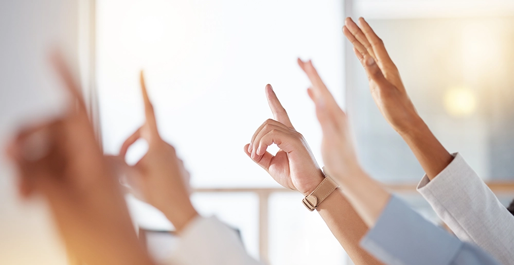 Diverse group of adults raising their hands at a community forum, symbolizing civic engagement and the importance of speaking up to protect Social Security’s future.