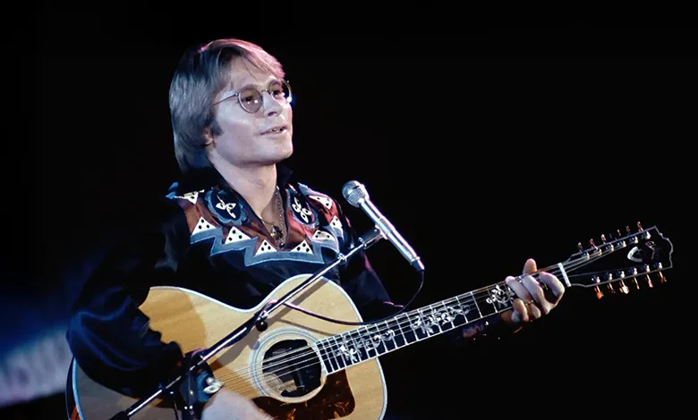 John Denver's 'Take Me Home, Country Roads' Hits 55 This Year 1 John Denver on stage playing guitar and singing